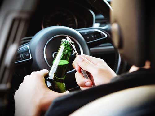 drunk driving opening a bottle behind the steering wheel of a car